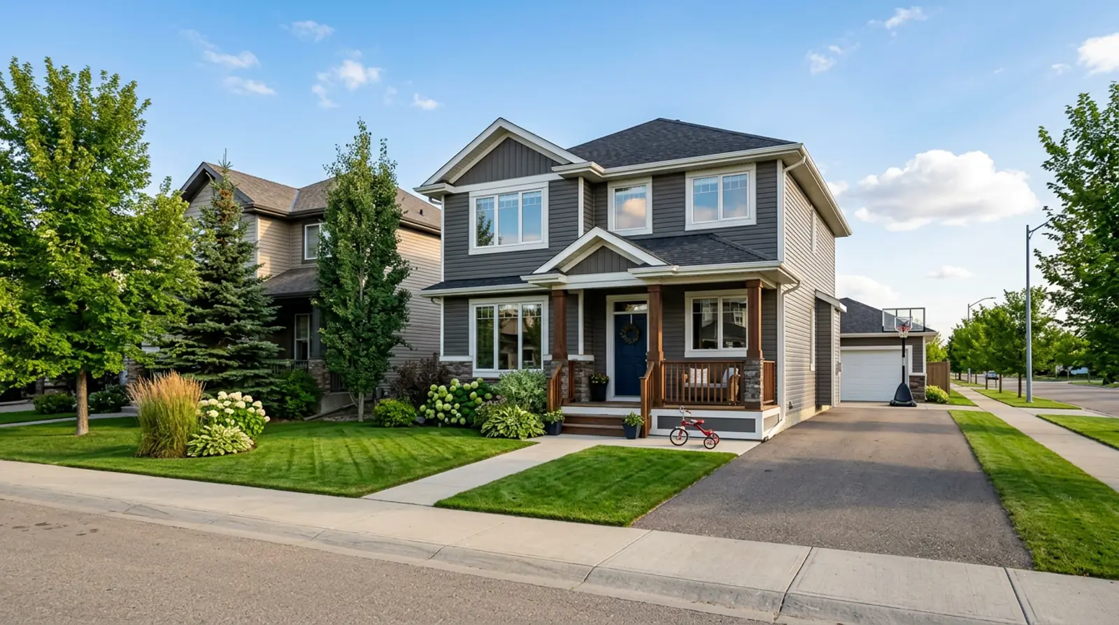 Modern Martensville family home with a tricycle by the porch and a basketball net at the driveway on a sunny afternoon.